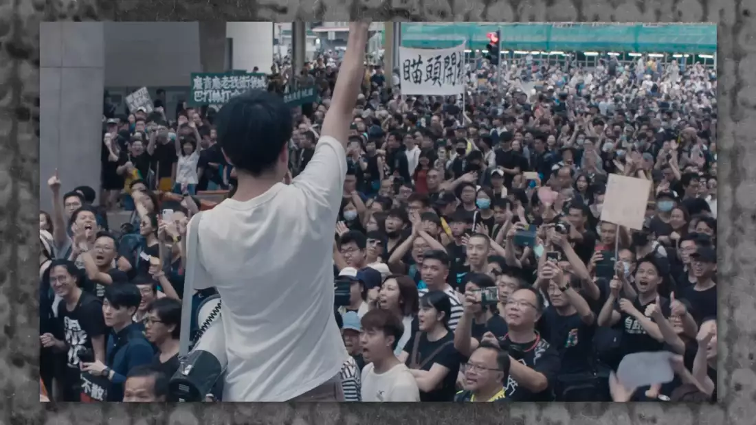 A still from Ai Weiwei's film Cockroach showing a speaker stood in front of a large crowd of people at a protest in Hong Kong