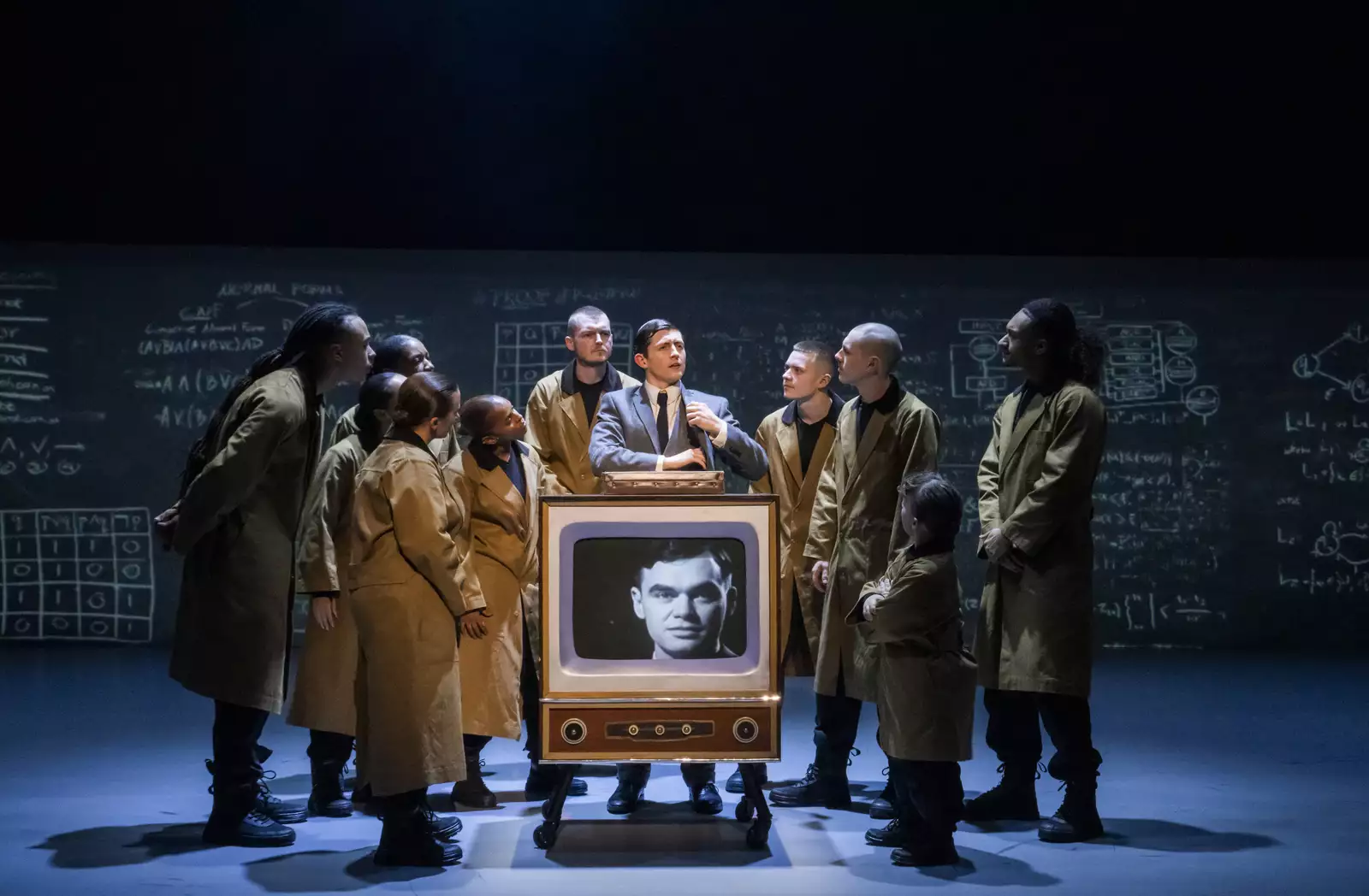 Dancers in brown trench coats stood around a TV in Free Your Mind