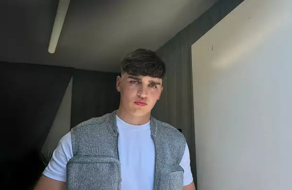 Tays stood in front of a white door wearing a white top and silver jacket