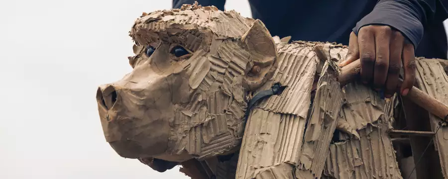 Close-up of a cardboard baboon puppet being operated by a person using wooden controls.