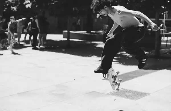 Black and white photograph of a skateboarder mid-trick wearing black adidas trainers
