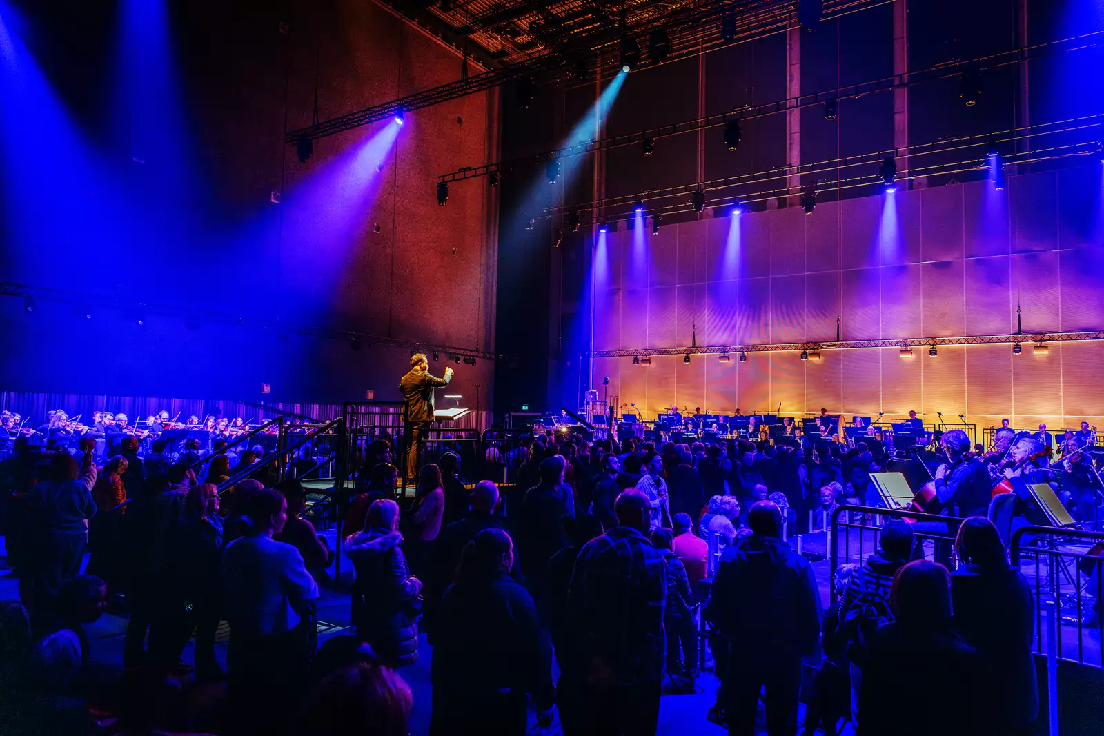A crowd of people stood in the Warehouse watching an orchestra