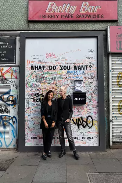 Mary Anne Hobbs and Anna Phoebe stood in front of the 'What do you want?' billboard, which is filled with text and graffiti