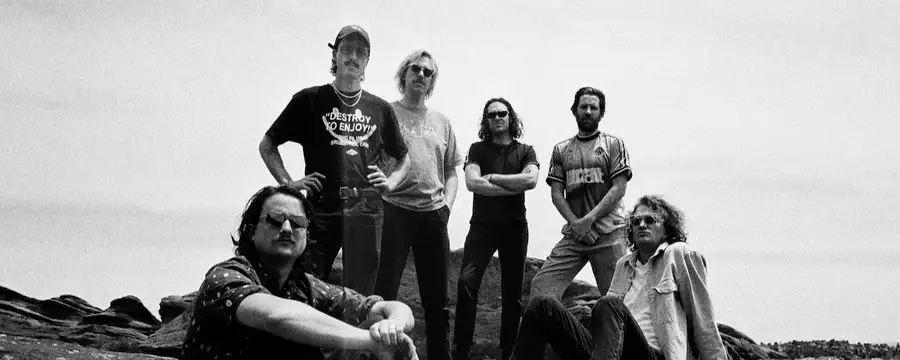 A black and white photo of six members of King Gizzard & The Lizard Wizard posing on a rocky landscape.