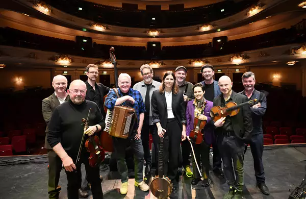 Members of Transatlantic Sessions stood on stage with their instruments. There is an empty auditorium behind them.