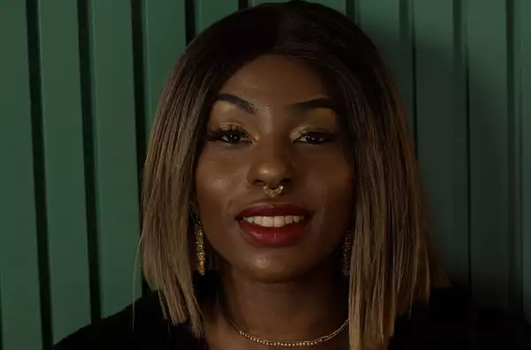 A young woman wearing red lipstick and a septum piercing smiles at the camera.