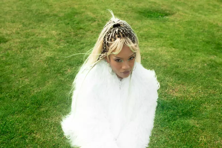 Cariss Auburn wearing a white fluffy coat, sat on green grass