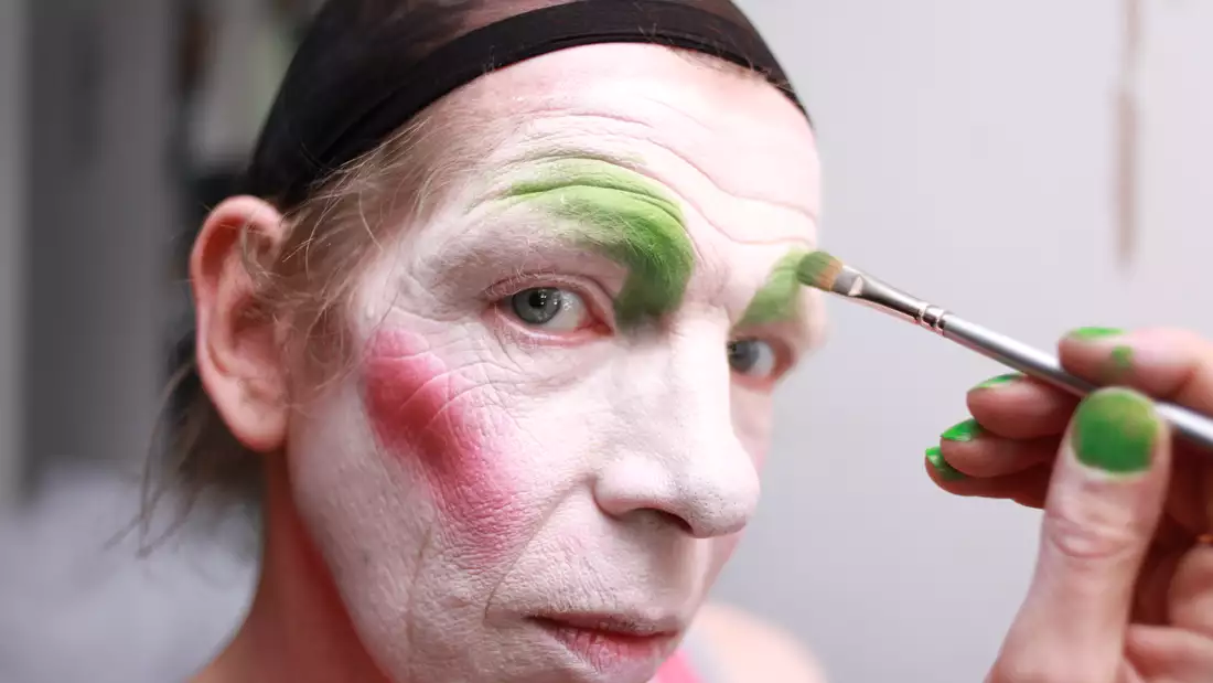 Close-up photo of David Hoyle having his face painted, looking at the camera