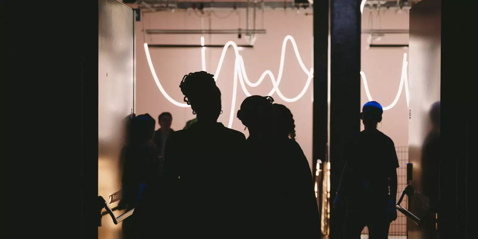 The outlines of people walking into the dark Warehouse – with bright lights in the stairway