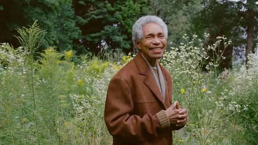 Glenn wearing a brown jacket and smiling, stood outside in a field of flowers