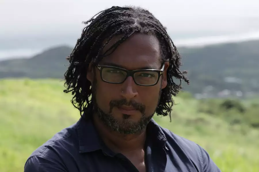Headshot of David Olusoga. The background is blurred and shows a green field and hills.