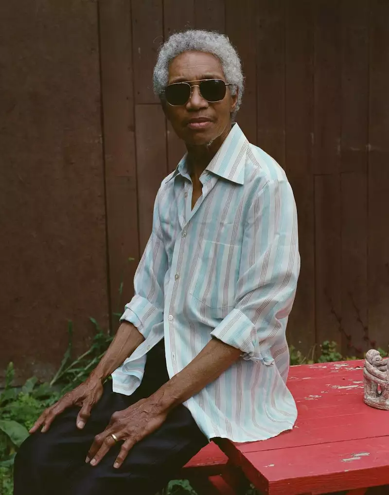 Glenn wearing sunglasses and a blue, pink and white shirt, sat on the bonnet of a red car