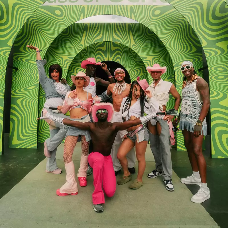 A group of people smiling and posing, wearing pink cowboy hats, stood in front of a bright, patterned green background