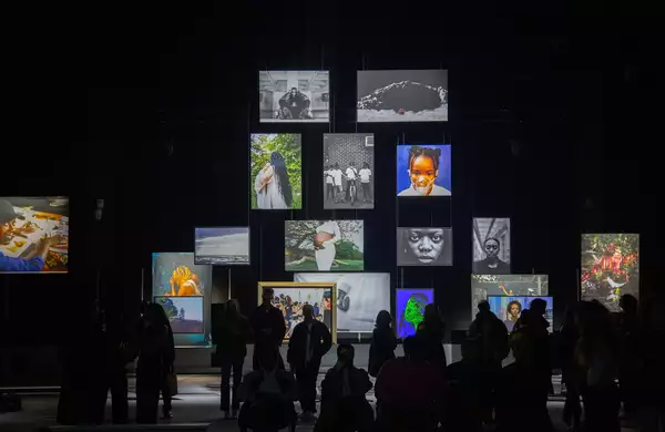 A group of people stood in the Reframe exhibition looking at the photographs, which are hanging from the ceiling of the Warehouse