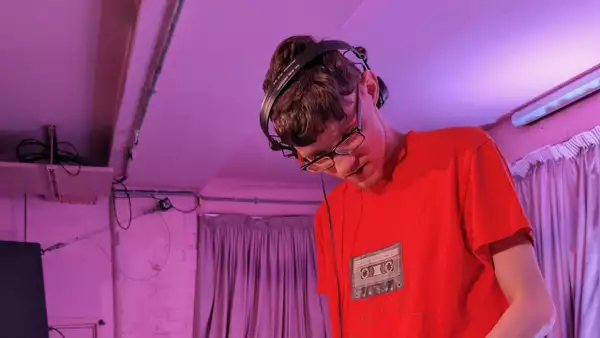 DJ Xanda DJing wearing a red top and headphones. The lighting is purple.