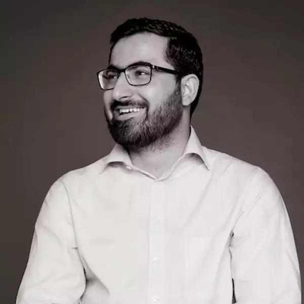 Black and white headshot of Gulwali Passarlay wearing a shirt, smiling and holding a book