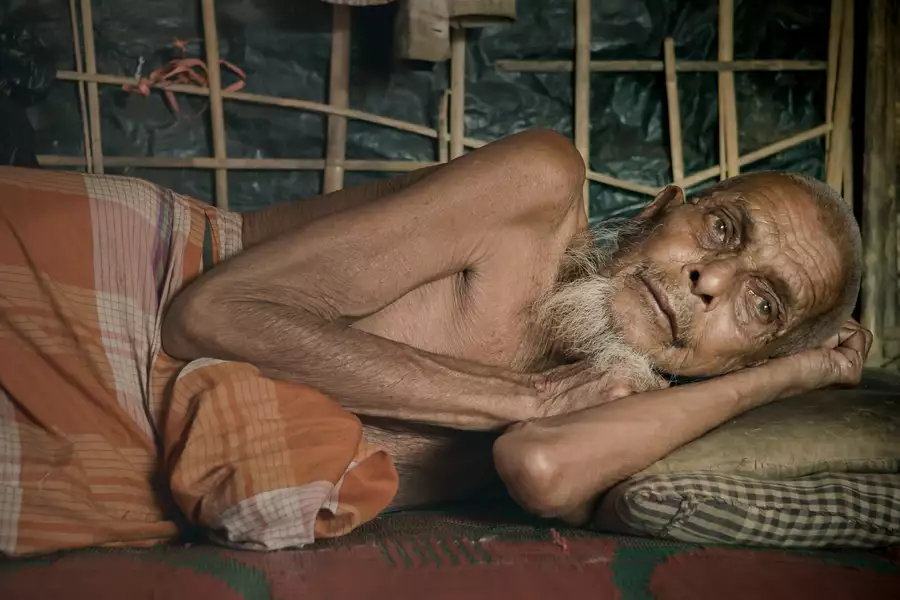 An old man lying down under a quilt, looking away from the camera