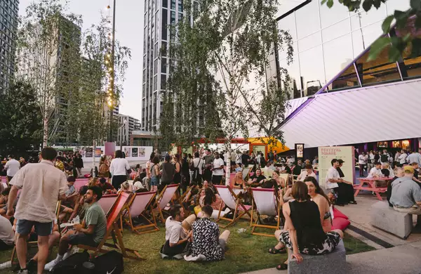 A large crowd of people sitting on deckchairs, smiling and drinking in Festival Square outside Aviva Studios
