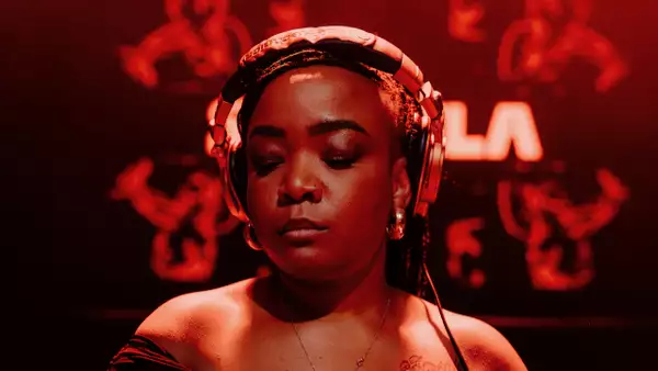 Artist Lebo wearing big headphones and looking down. The lighting is red.
