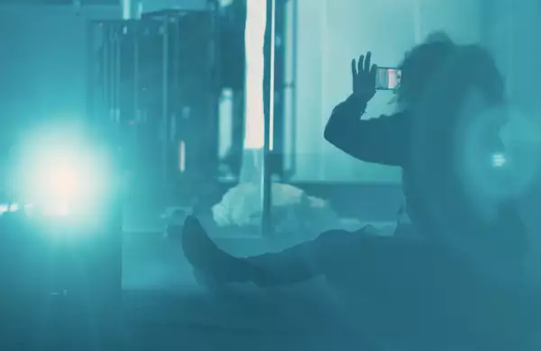 Juliet Ellis taking a photo sat on the floor, in a blue-lit, smoky environment.