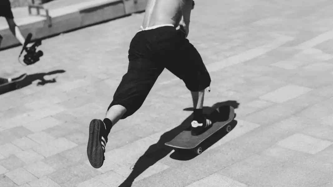 Black and white photograph of a skateboarder skating wearing black adidas trainers