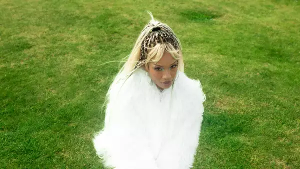 Cariss Auburn wearing a white fluffy coat, sat on green grass