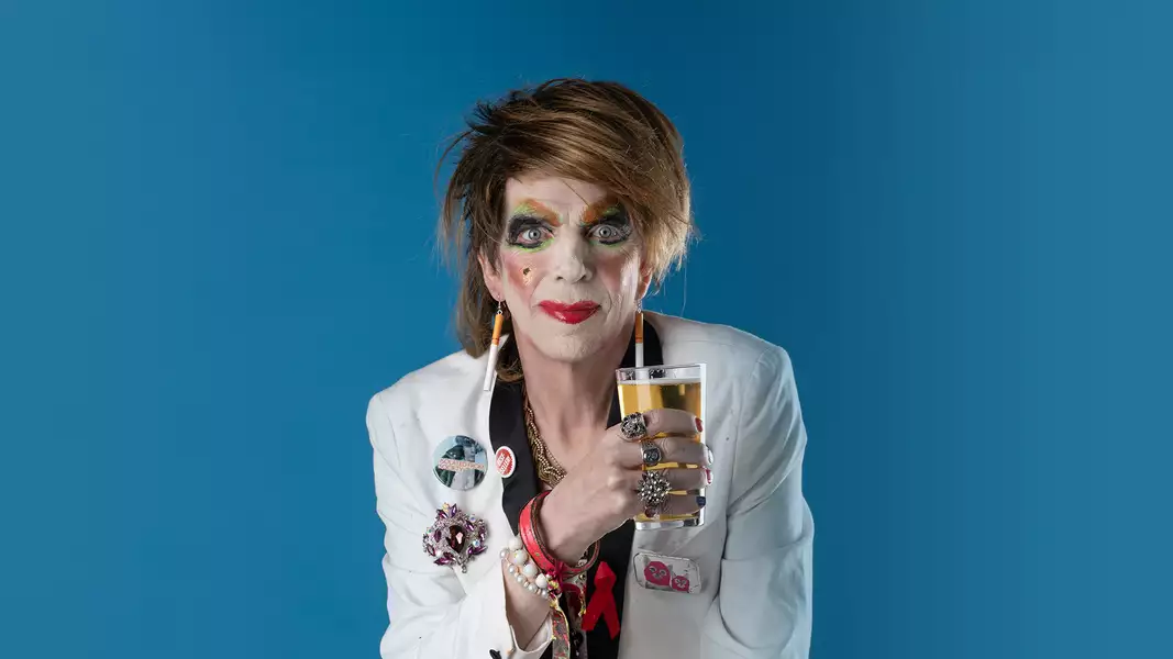 David Hoyle holding a pint glass on a blue background