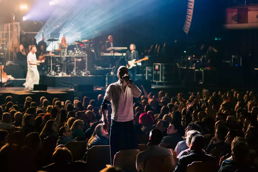 Lead singer of JAMES singing in the middle of a large crowd, with the band behind on stage