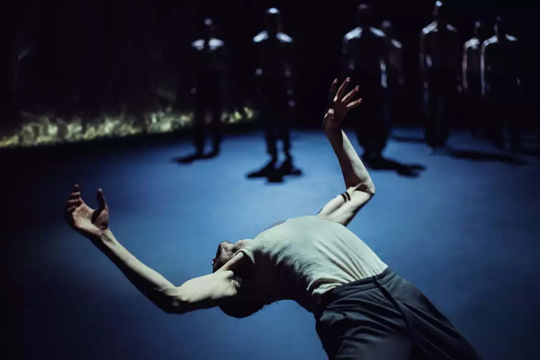 A still from Figures in Extinction [1.0] showing a dancer leaning backward under low light, with silhouetted figures in the background.