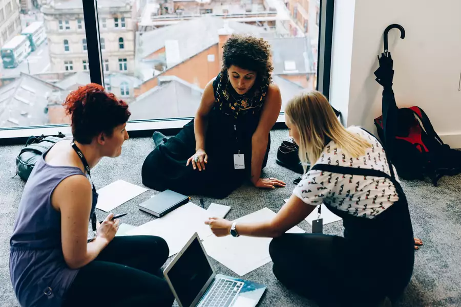 Three women sat on the floor surrounded by paper and laptops, working together on a project