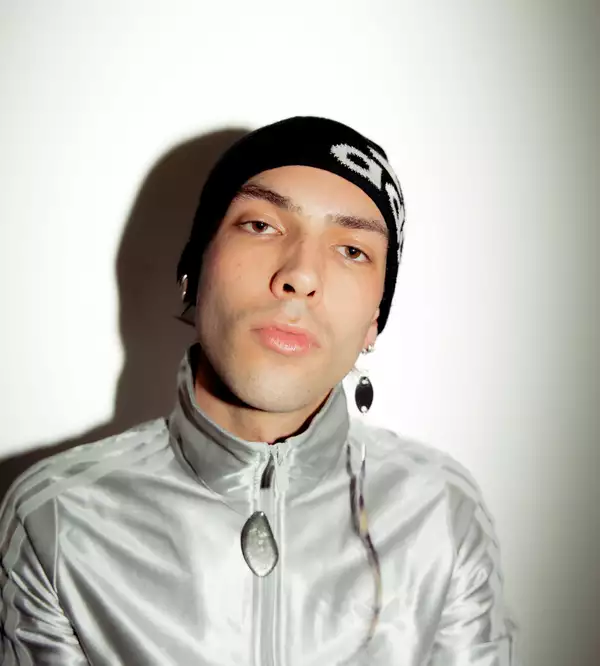 Jack Jameson wearing a silver velvet Adidas hoodie and a black hat, on a white background