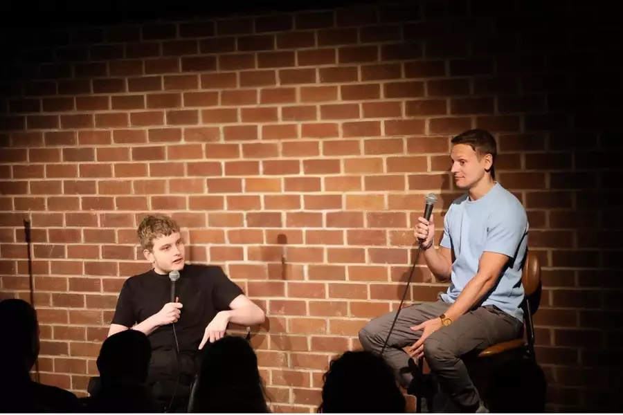 Wheels and the Legman performing on stage holding microphones. Behind them is a brick wall.