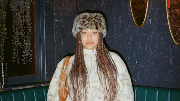 mamba exe. wearing a fluffy leopard print hat, white zipped jumper and a brown bag