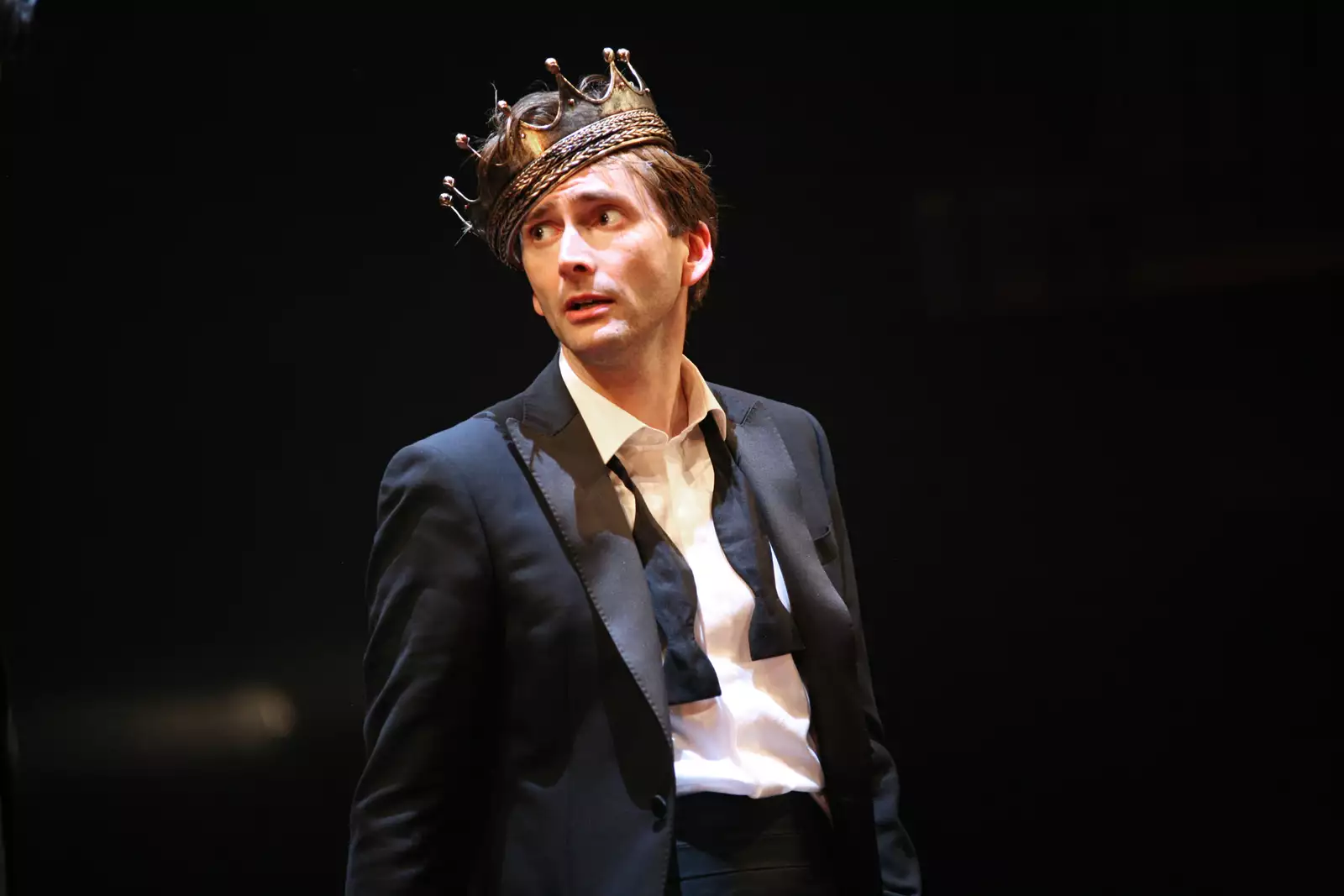 David Tennant dressed as Hamlet wearing a suit jacket, untied bow tie and lopsided gold crown