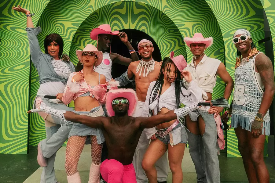 A group of people smiling and posing, wearing pink cowboy hats, stood in front of a bright, patterned green background