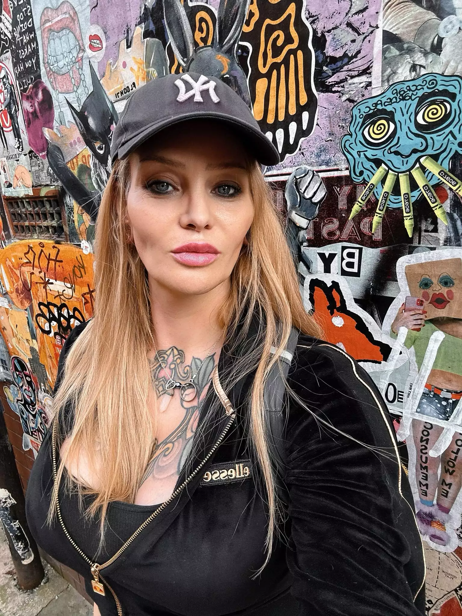 Photo of Kim Lana wearing a black cap, stood in front of a mural