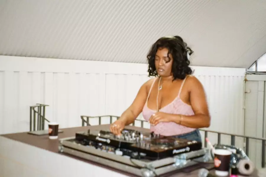 Zeyla DJing in a white room wearing a pink top