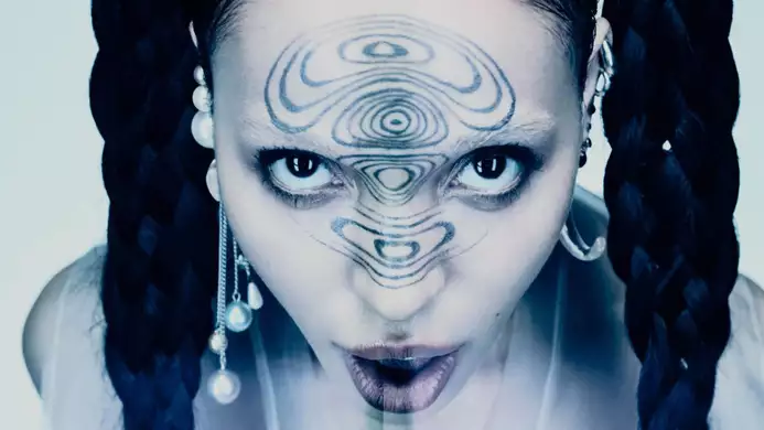 A surreal portrait of FKA Twigs with braided hair, pearl earrings and intricate patterns painted on her forehead.