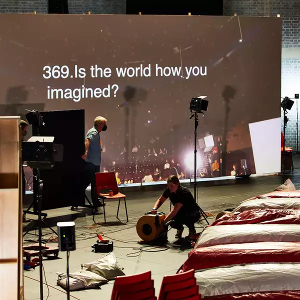 Photograph of a stage being set up with a screen that says '369. Is the world how you imagined?'
