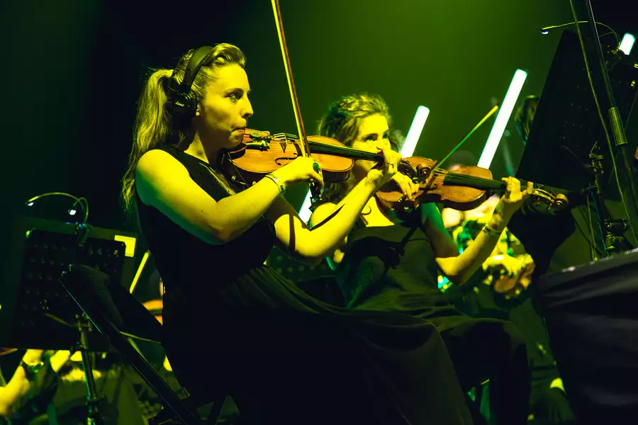 Close-up shot of two performers playing violin in yellow lighting