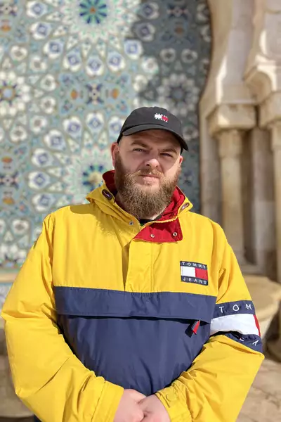 Daniel Son wearing a yellow and blue jacket in from of a mosaic wall