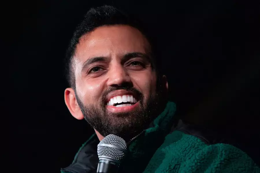 Akaash Singh speaking into a microphone on a black background, wearing a green fleece