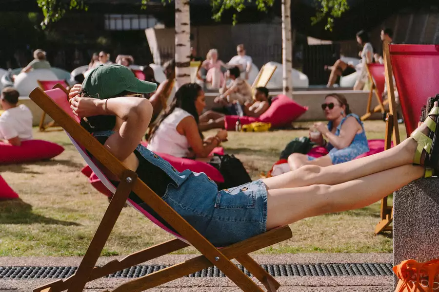 A person relaxing on a pink deck chair on grass outside Aviva Studios