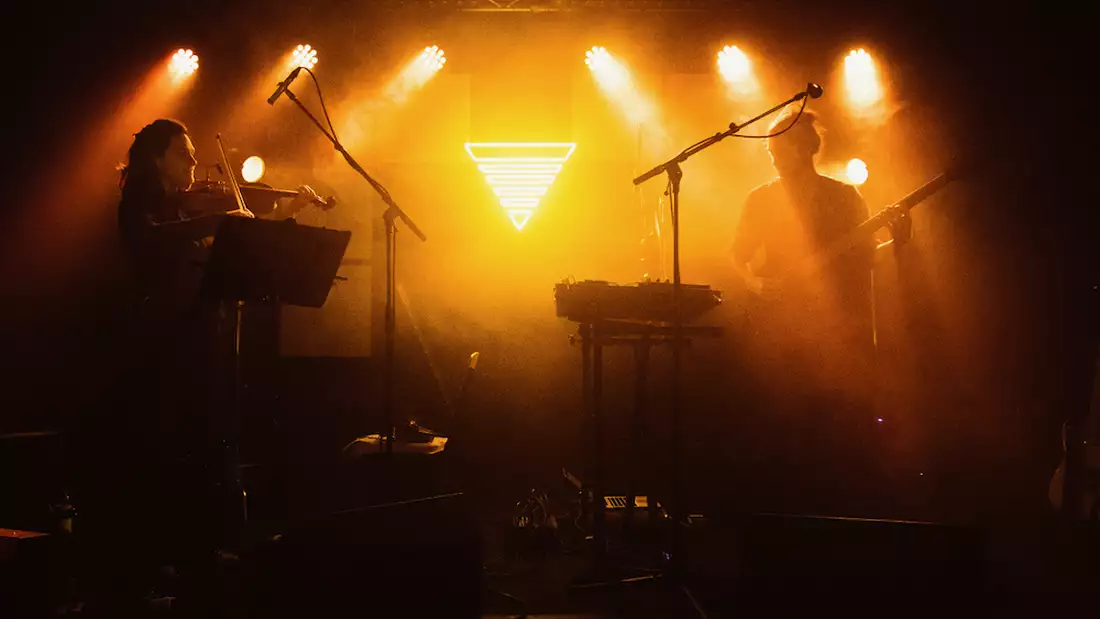 Two members of Manchester Collective performing on a stage with hazy yellow lighting