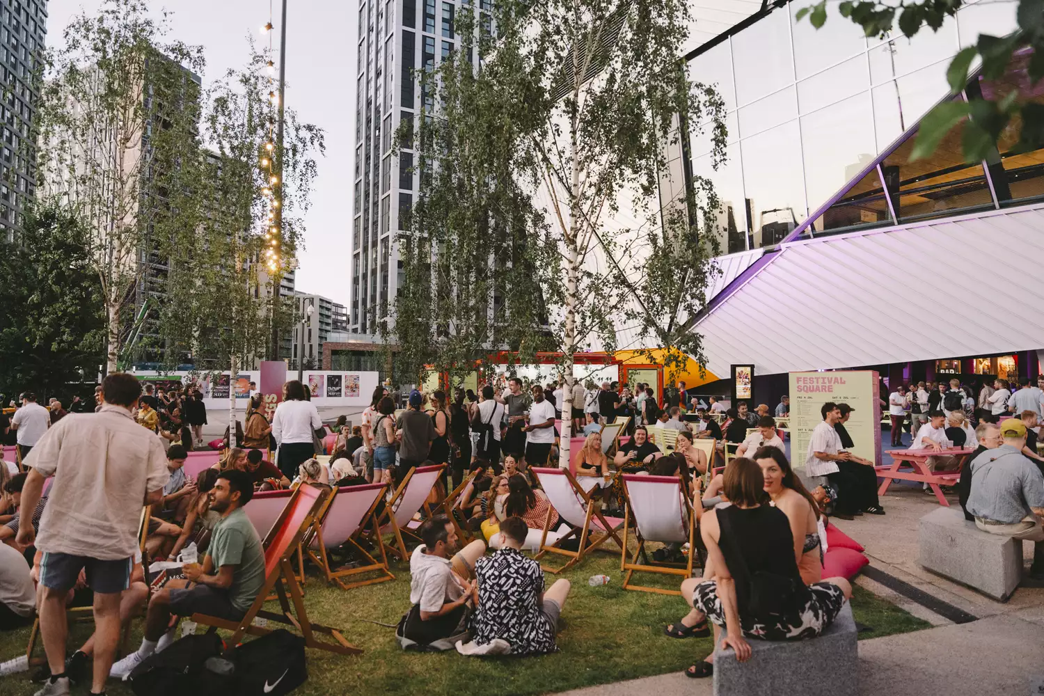 A large crowd of people sitting on deckchairs, smiling and drinking in Festival Square outside Aviva Studios