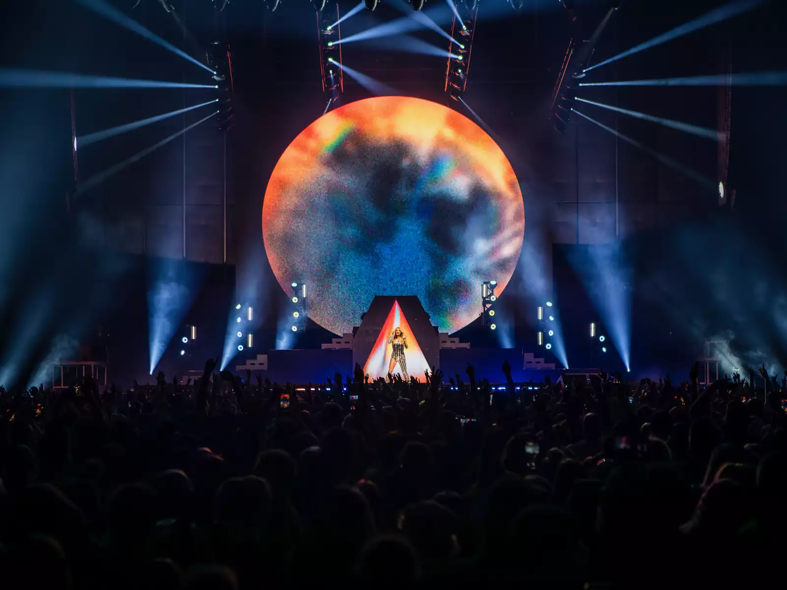 Kesha on stage in the Warehouse with a huge crowd watching. She is singing with a giant moon behind her.