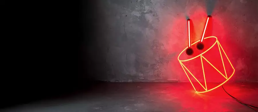 Neon red drum sign with drumsticks leaning against a concrete wall.