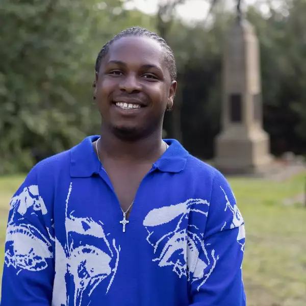 Headshot of Demereece Green wearing a bright blue and white shirt. They are stood outside in a park.