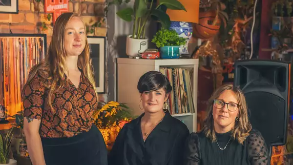 Three members of Canter Semper smiling. Behind them are lots of records.