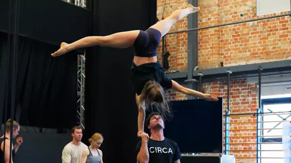 A Circa acrobat doing the splits upside down, balancing on another acrobat's hand